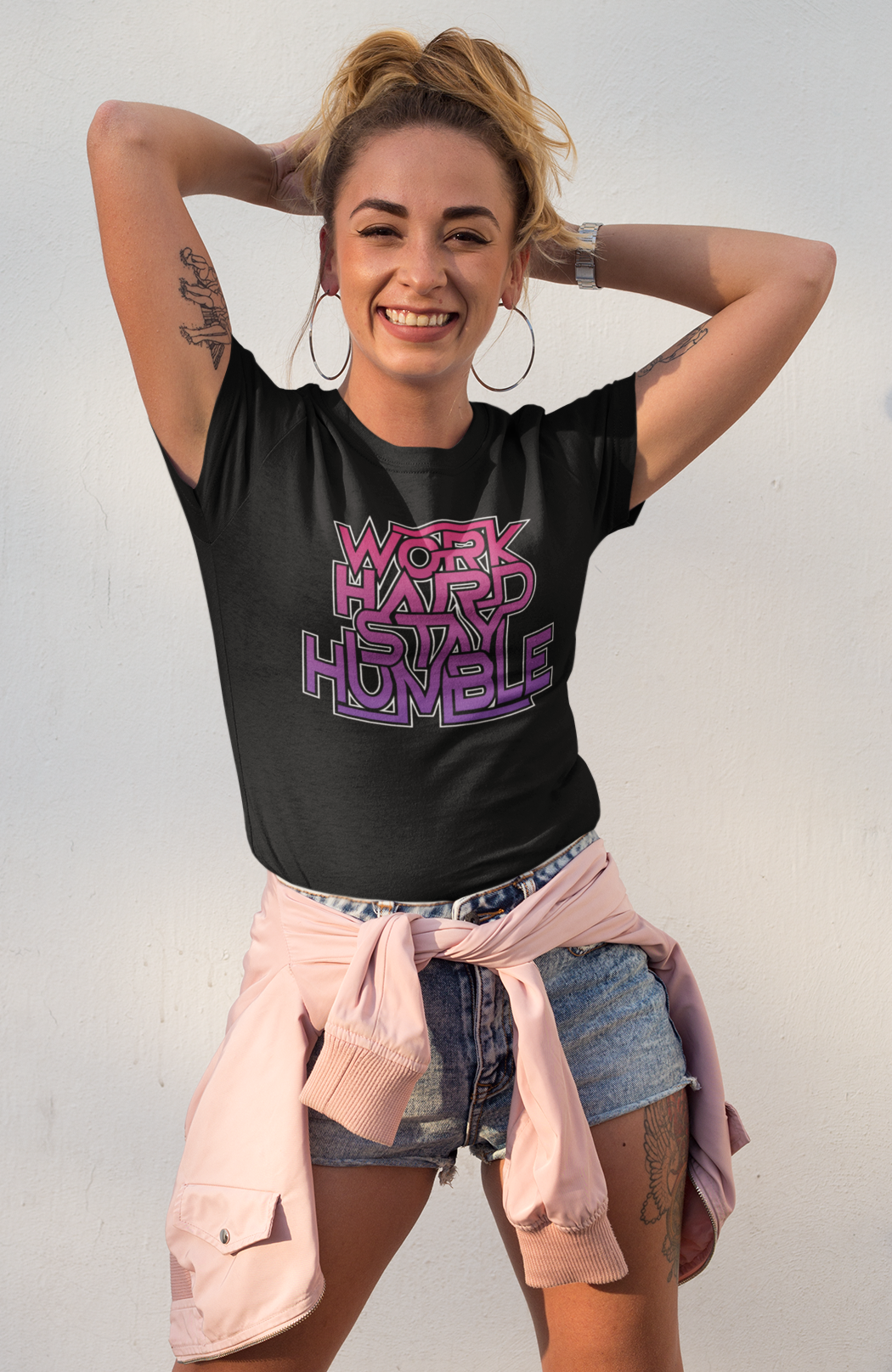 Woman wearing a black t-shirt with pink text, standing against a light gray background