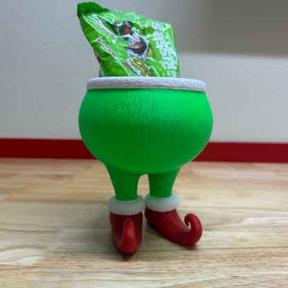 Green elf figurine with a small green bag on its head against a plain wall.