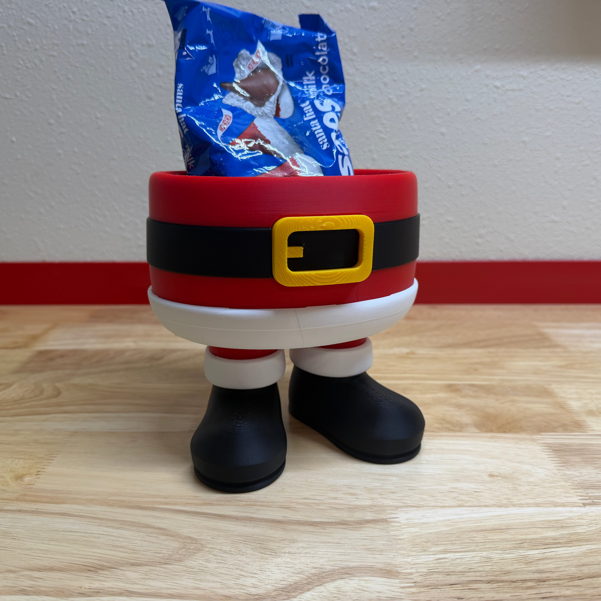 Santa Claus-themed candy bowl with a bag of candy on a wooden surface.