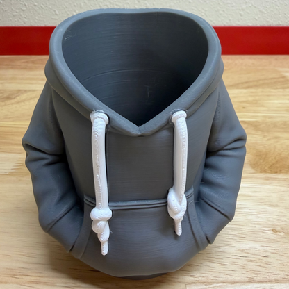 Gray hoodie-shaped container on a wooden floor with a white wall background