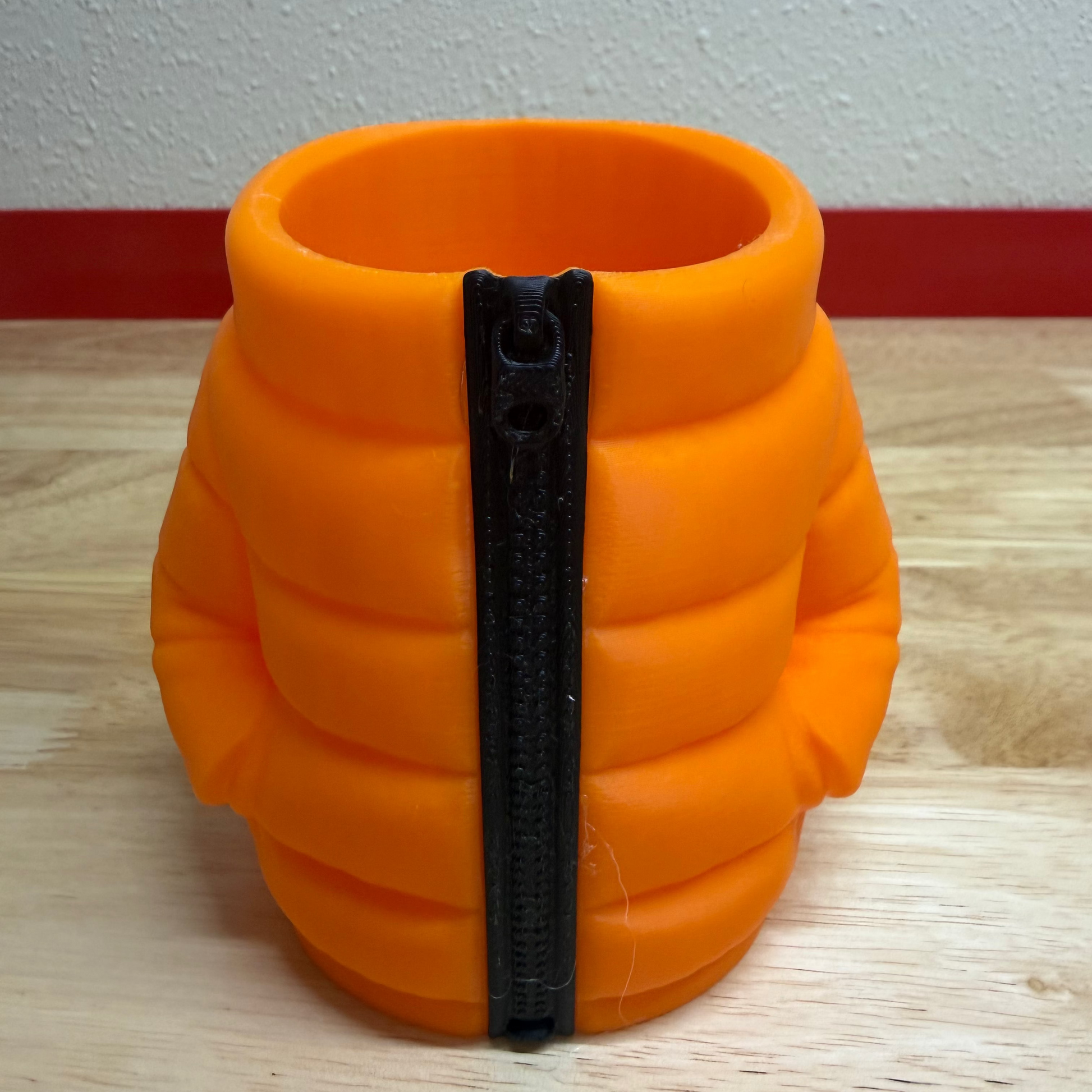 Orange container shaped like a puffer jacket with a black zipper on a wooden surface.