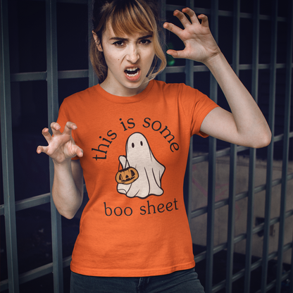 Person wearing an orange t-shirt with a ghost and pumpkin design, standing in front of a dark metal fence.