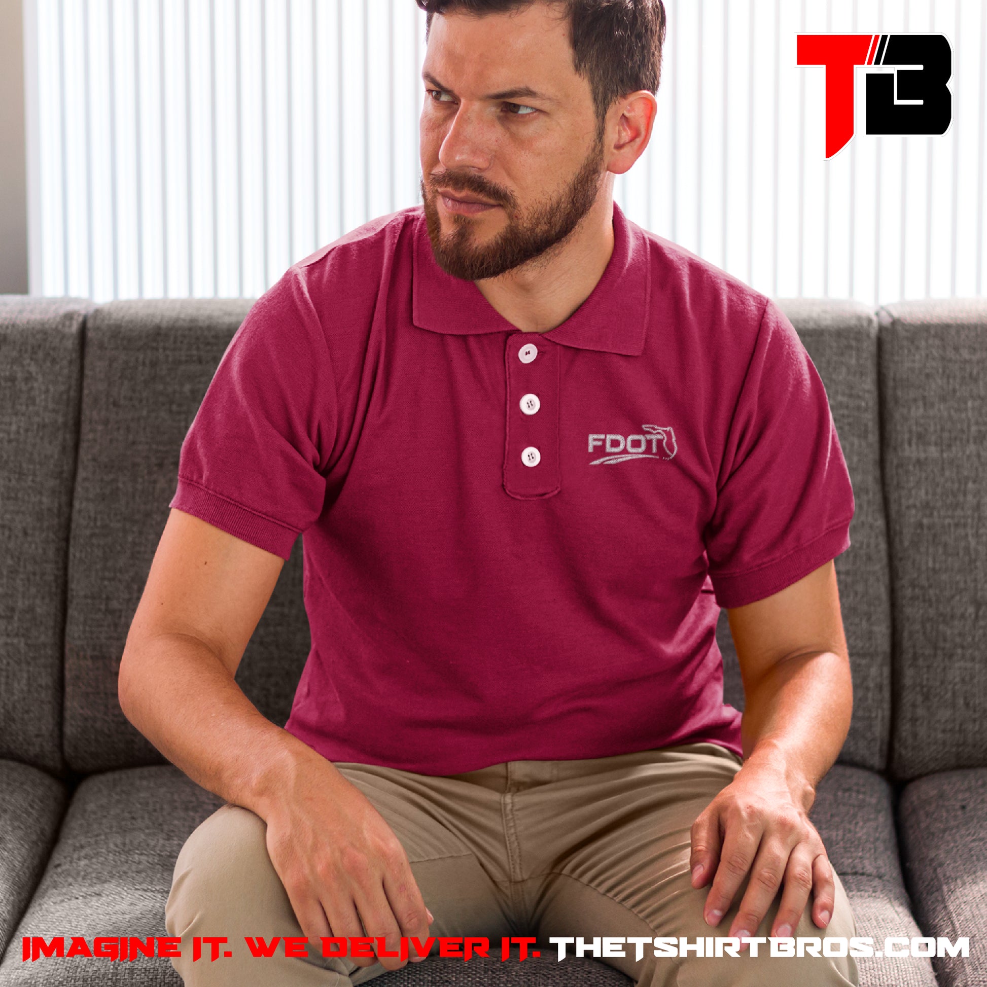 Man wearing a maroon polo shirt with a logo, sitting on a gray couch.