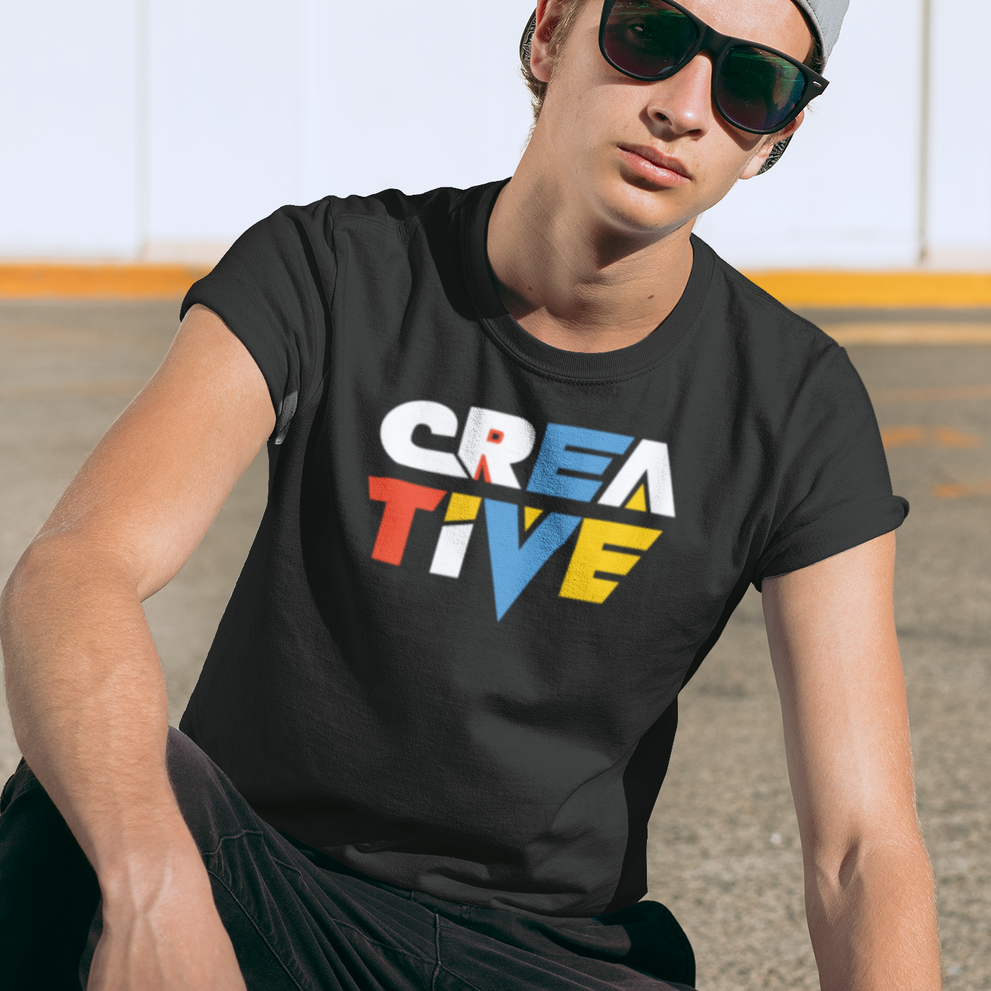 Person wearing a black t-shirt with 'CREATIVE' in colorful letters, sitting outdoors.