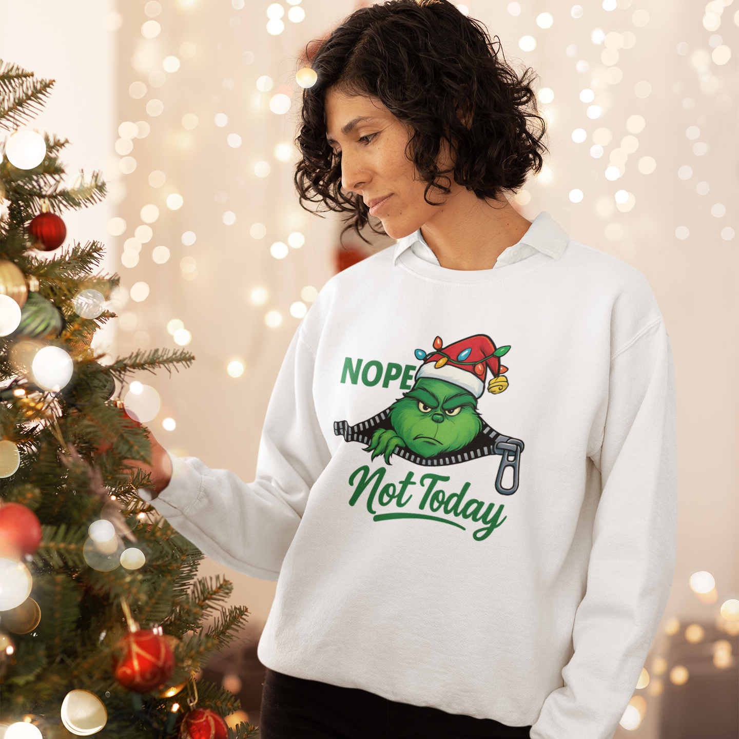 Person wearing a white sweatshirt with a Christmas-themed design, standing next to a decorated Christmas tree.