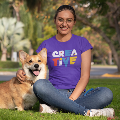 Woman sitting on grass with a dog, wearing a purple 'CREATIVE' t-shirt