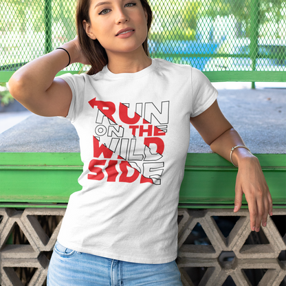 Woman wearing a white t-shirt with 'Run on the Wild Side' text, standing against a green metal fence.